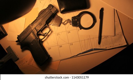 Overhead Shot Of A Police Officer's Work Desk With A Gun, Handcuffs, Wallet, And Notepad