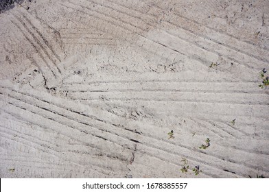 An Overhead Shot Of A Sandy Surface With Tire Marks And Small Stems