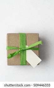 Overhead shot of a simple brown gift box, with green raffia ribbon and blank label on white background. - Shutterstock ID 509446333