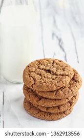 Overhead Shot Of Stack Of Fresh Homemade Oatmeal Cookies With A Bottle Of Milk On A White Table Against A White Background..