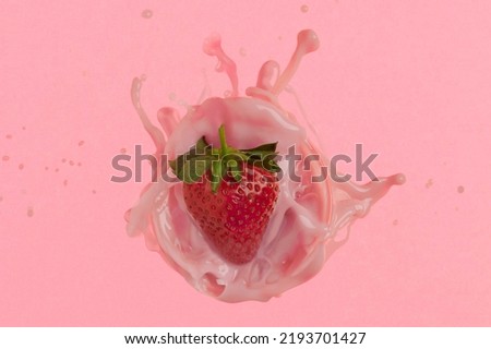 Overhead shot of a strawberry creating a splah in a glass full of milk on a pink background