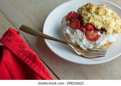 Overhead Shot Of A Strawberry Shortcake With A Fork And Red Cloth Napkin On A Wooden Table.  