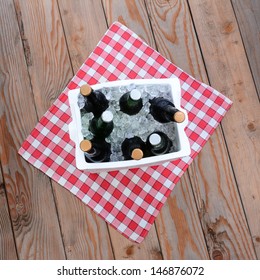 Overhead Shot Of A Styrofoam Ice Chest Full Of Beer Bottles On A Red And White Checked Table Cloth On A Wood Deck. Square Format.