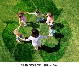 Overhead shot of teacher with five young students in a circle forming a human chain play on a green lawn outdoors with overlay of recycle symbol. - Powered by Shutterstock