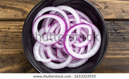 Overhead shot of thinly sliced red onion rings in a dark bowl. Perfect for recipes or culinary backgrounds.