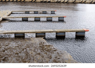 Overhead shot of three parallel empty wooden pontoons or docks stretching over dark water, with a section of murky algae-covered water below.