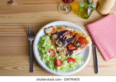 Overhead Shot Of A Vegetarian Pizza And Salad, With Cutlery, Napkin, Wine And Condiments, Set Out On A Pine Wooden Slatted Table.