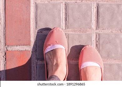 An Overhead Shot Of A Woman's Feet In Orange Shoes Walking On A Gray Brick Road