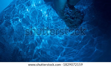 An overhead shot of a woman's feet submerged in blue water in a tub