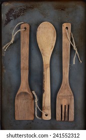 Overhead Shot Of Wooden Kitchen Utensils, Fork, Spoon, And Spatula, With Twine Through The Handle Hole On A Used Metal Baking Sheet. Vertical Format With Middle Spoon Inverted..