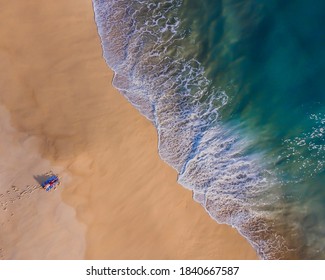 Overhead Shot Of Young Adult Laying On The Beach With The Waves Getting Close