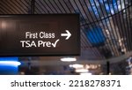 Overhead sign showing security check point lanes designated for first class and TSA Precheck passengers. Illuminated white text on black banner. Silver metallic ceiling in bokeh in background.
