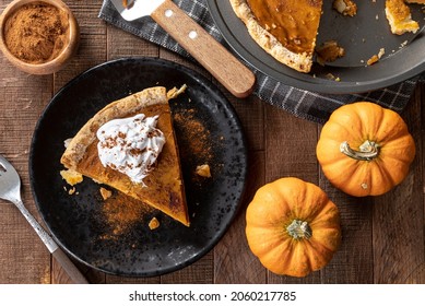 Overhead Of Slice Of Pumpkin Pie With Whipped Cream And Cinnamon With Pumpkins On A Wooden Table