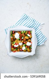 Overhead Of Spicy Southwestern Casserole With Tater Tots, Fresh Diced Avocado And Dollops Of Rich Sour Cream In Square, White Casserole Dish Over Aqua Striped Linen And Cream Marble Surface.