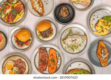 Overhead Spread of Brunch Plates Featuring Burgers, Toasts, Croissants, and Eggs on Metal Trays