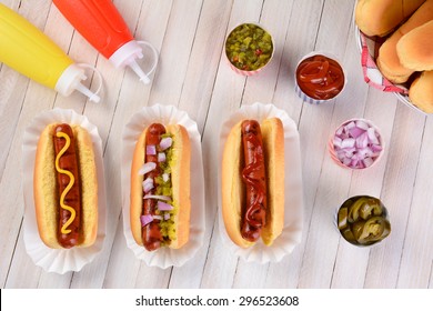 Overhead still life of a summer picnic table with hot dogs and condiments. Three franks in buns with ketchup, mustard, and relish surrounded by condiments. - Powered by Shutterstock