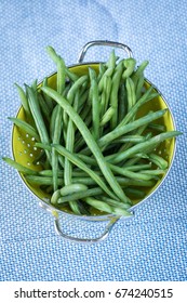 Overhead Top Down Perspective Of Freshly Washed And Trimmed Organic Green String Beans From Farmers Market Arranged In Small Yellow Colander And Blue Pattern Linen Table Cloth In Editorial Food Scene