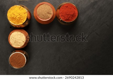 Overhead top view flat lay colourful array of spices herbs powder blue clay ceramic brass metal pot on dark black slate surface with a clean and neat appearance spice copy text space border frame 