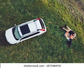 Overhead Top View Of Suv Car And Couple Laying Down On A Blanket At River Beach