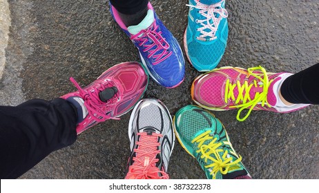 Overhead view of 6 brighlty colored runners' shoes on wet pavement