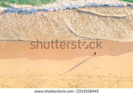 Overhead view of alone man walking by the white sandy beach along the amazing clear light blue ocean. Aerial view of a walking man on a beach, lonely on the sand with beautiful view of waves.