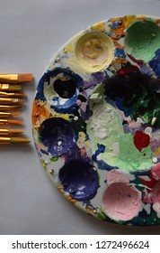 An Overhead View Of An Art Palate With Dried Paint In Various Colors Next To Paint Brush Tips.