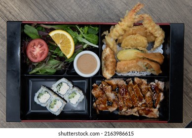 Overhead View Of Asian Cuisine Traditional Bento Box Divided Into Space For The Teriyaki Chicken, Krab Roll, Vegetable Tempura, And Garden Salad.