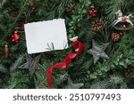 Overhead view of assorted branches of coniferous trees with Christmas ornaments and white paper card mock up for a festive Christmas background.