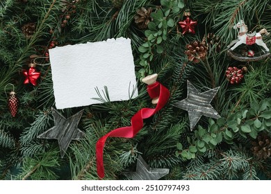 Overhead view of assorted branches of coniferous trees with Christmas ornaments and white paper card mock up for a festive Christmas background.