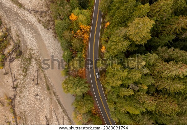 Overhead View of an Automobile Traveling on a Roadway\
Next to a River During the Fall Season. A car travels along the\
colorful, autumnal, Mt. Baker Highway alongside the beautiful\
Nooksack River. 