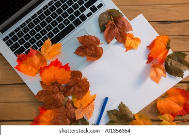 Overhead view of autumn leaves with paper by laptop on wooden table - Powered by Shutterstock