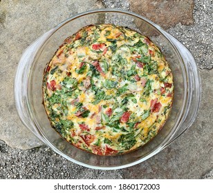 Overhead view of a baked crustless quiche in a pyrex baking dish with melted cheddar, tomatoes, ham, and spinach