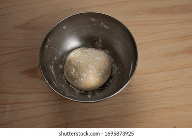 Overhead View Of A Ball Of Pizza Dough With Flour In An Iron Bowl On A Wooden Table