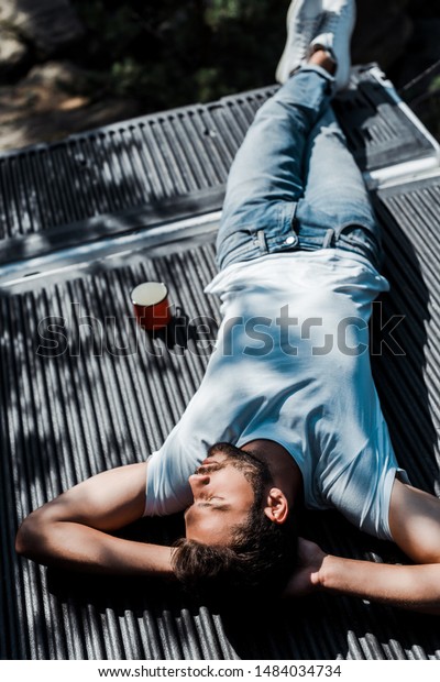 overhead view of bearded man lying with closed eyes
near cup
