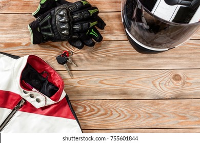 Overhead view of biker accessories placed on rustic wooden table. Items included motorcycle helmet, gloves, keys and jacket. Motorcycle travel dream concept.