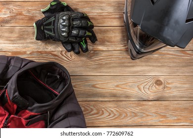 Overhead view of biker accessories placed on rustic wooden table. Items included motorcycle helmet, gloves and jacket. Motorcycle travel dream concept.