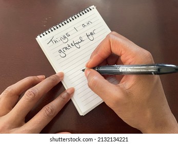 An Overhead View Of A Black Person Holding A Pen And Writing A Gratitude List On A Notepad