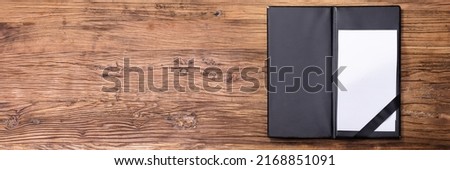 Overhead View Of Blank Empty White Paper In Black Leather Folder On Wooden Table