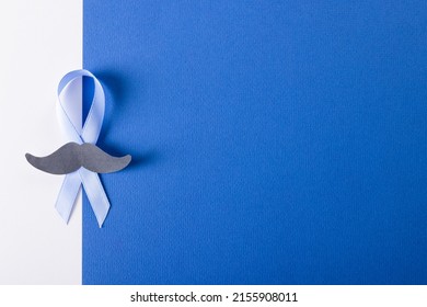 Overhead view of blue prostate cancer awareness ribbon with paper mustache on blue, white background. copy space, prostate, cancer, mustache, medical, awareness, support, healthcare and alertness.