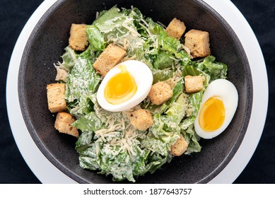 Overhead View Of Bowl Of Caesar Salad With Topped With Parmesan Cheese, Croutons, And Hard Boiled Egg.