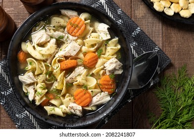 Overhead View Of A Bowl Of Chicken Noodle Soup With Carrots And Dill  On A Wooden Table