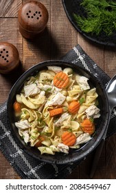 Overhead View Of A Bowl Of Chicken Noodle Soup With Carrots And Dill  On A Wooden Table