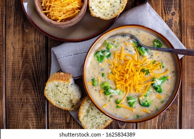Overhead View Of A Bowl Of Creamy Broccoli Cheddar Soup With Toasted Cheese Bread On A Wooden Table