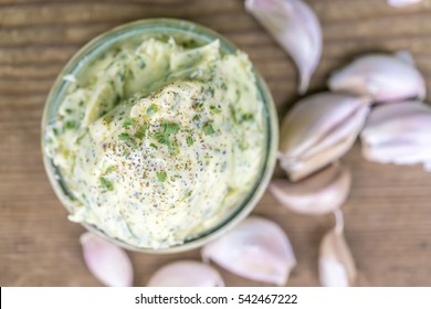 Overhead View Of Bowl Of Garlic Butter And Garlic Cloves On Wooden Table