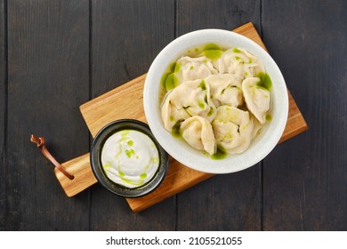 Overhead View Of A Bowl With Pork Pelmeni With Sour Cream On A Wooden Serving Board