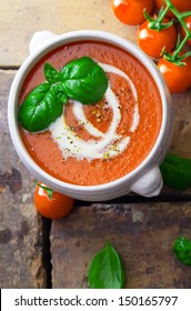 Overhead View Of A Bowl Of Tomato Soup Drizzled With Cream And Garnish With Leaves Of Fresh Green Basil