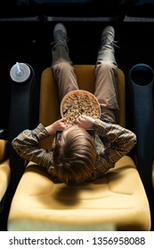 Overhead View Of Boy Eating Popcorn While Sitting In Cinema Chair Near Paper Cup