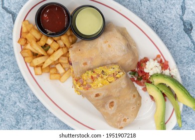 Overhead view of breakfast burrito is cut in half to reveal the loaded ingreadients of eggs and meat.