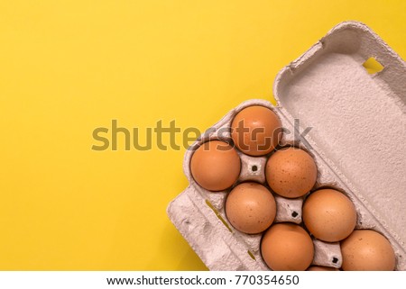 Overhead view of brown chicken eggs in an open egg carton isolated on yellow. Fresh chicken eggs background.  Top view with copy space. Natural healthy food and organic farming concept. Eggs in box