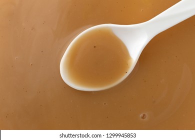 Overhead View Of Brown Creamy Turkey Gravy With A White Spoon In The Food.